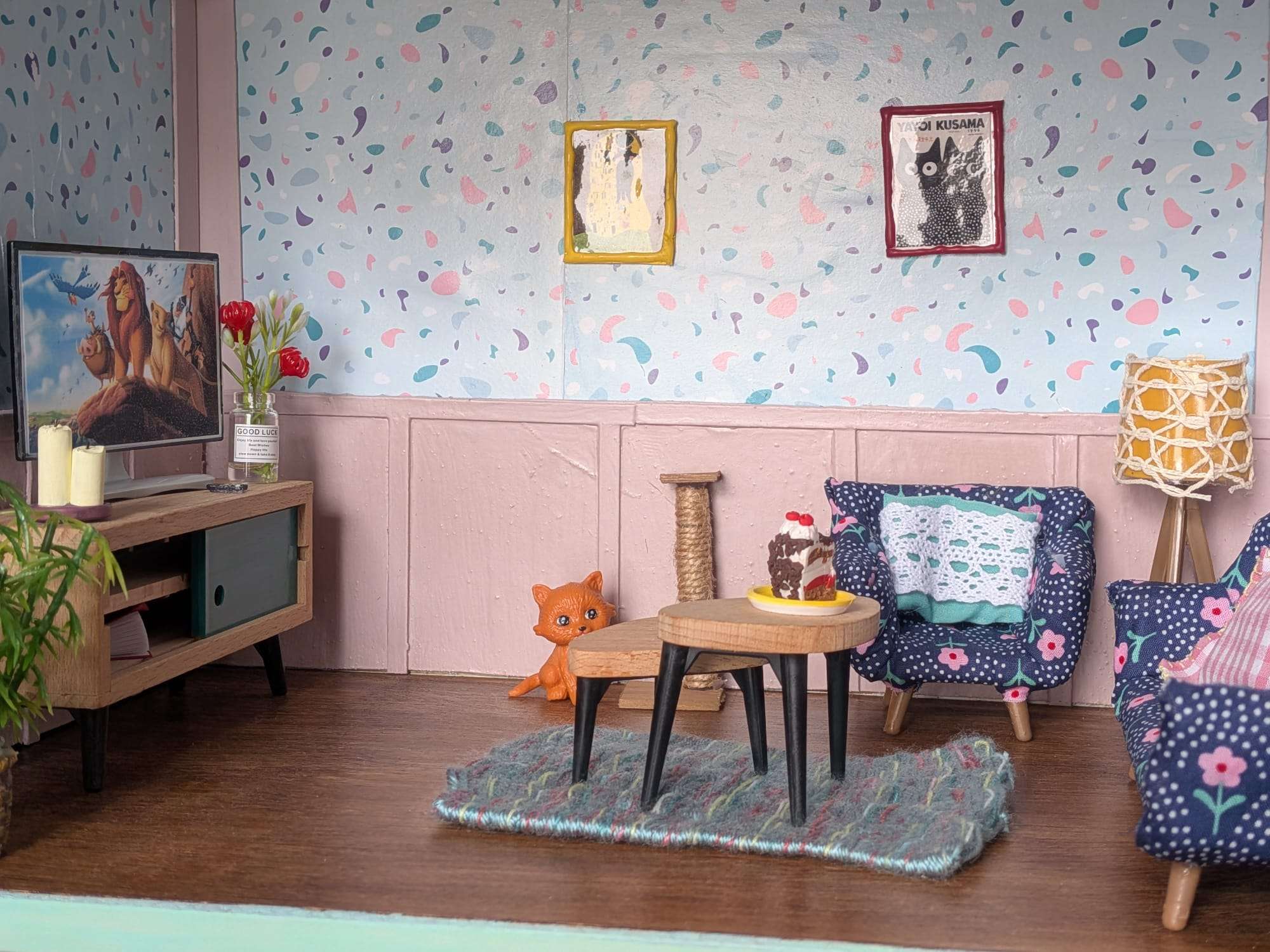 Sala em miniatura com poltronas floridas, mesa, televisão e gato